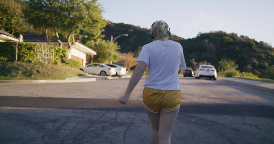 We follow from behind our character in workout clothes as she walks up a hill.