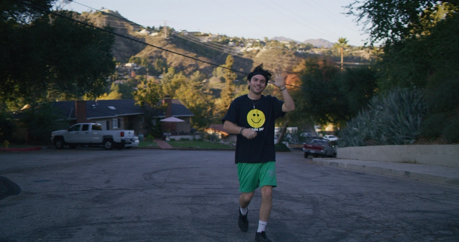 A jogger waves to our character as he approaches her at the top of a hill, and the Los Angeles hills are illuminated behind him.