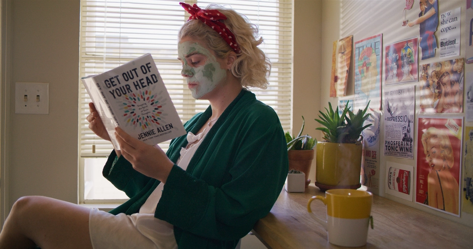 Our character sits in her kitchen reading a book called Get Our Of Your Head