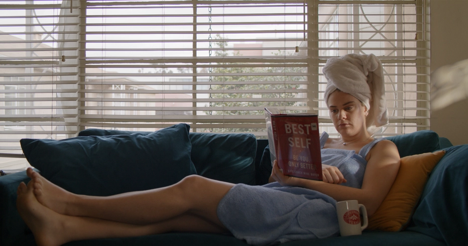 Our character on the couch reading a book called Best Self, she is softly backlit by the window behind her.