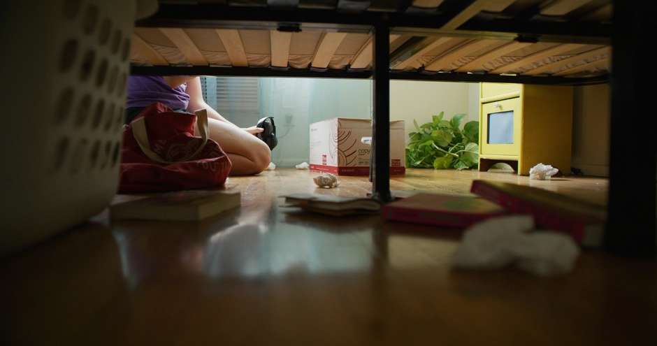 A moody angle from under the bed showing our main characters tissues on the ground while she sits between them.