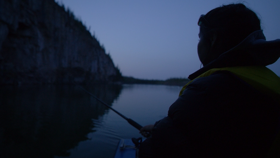 A young Dene woman fishes off the boat