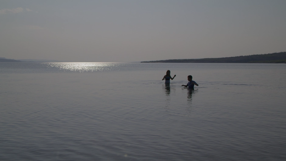 Two young kids play in the lake at sunset