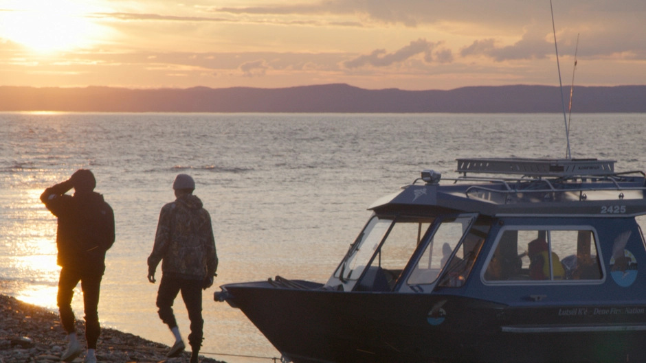 The boat sits on the shore in front of a sunset